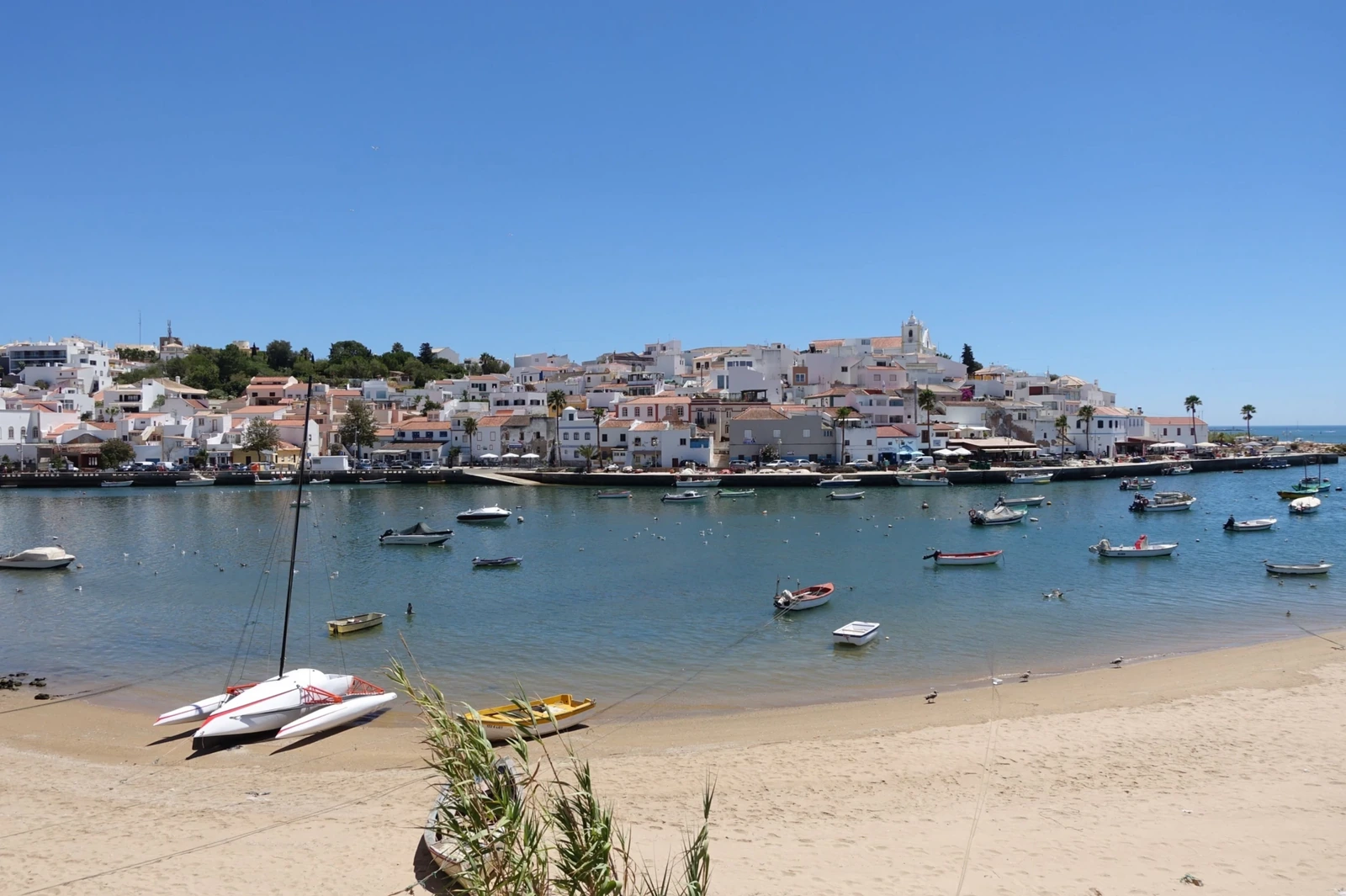 Frente ribeirinha de Ferragudo, com casario branco, igreja e barcos no Arade.